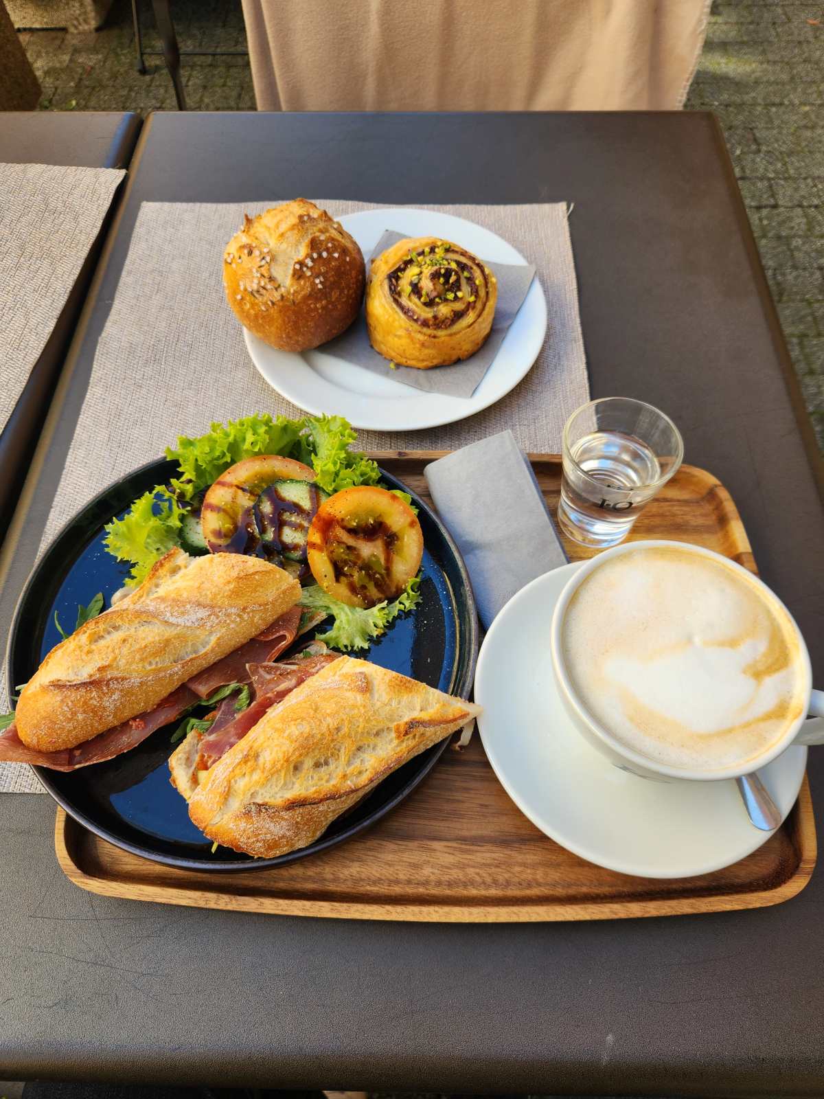 Cappuccino mit Schwarzwälder-Schinken-Sandwich, Weckle und Pistazien-Nuss-Rolle